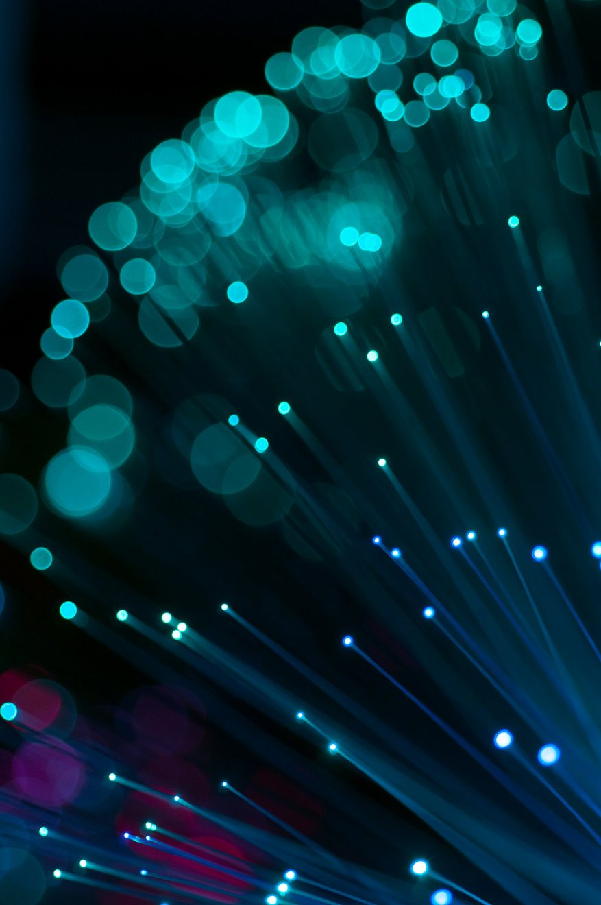 Fanned strands of fibre optic filament glowing turquoise against a black background