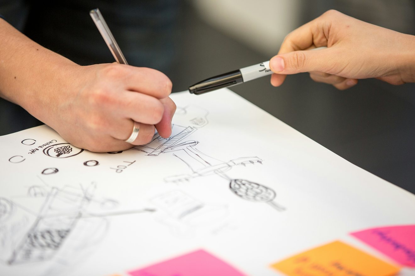 Two people at a table marking up a sheet of product concept sketches, one passing a marker pen across