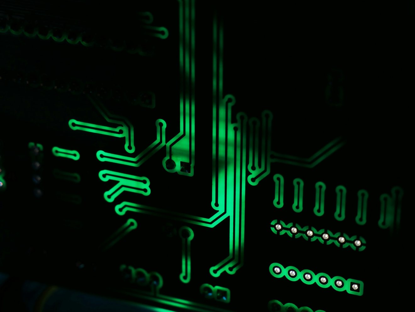 Green illuminated copper tracks running across a dark printed circuit board in close-up